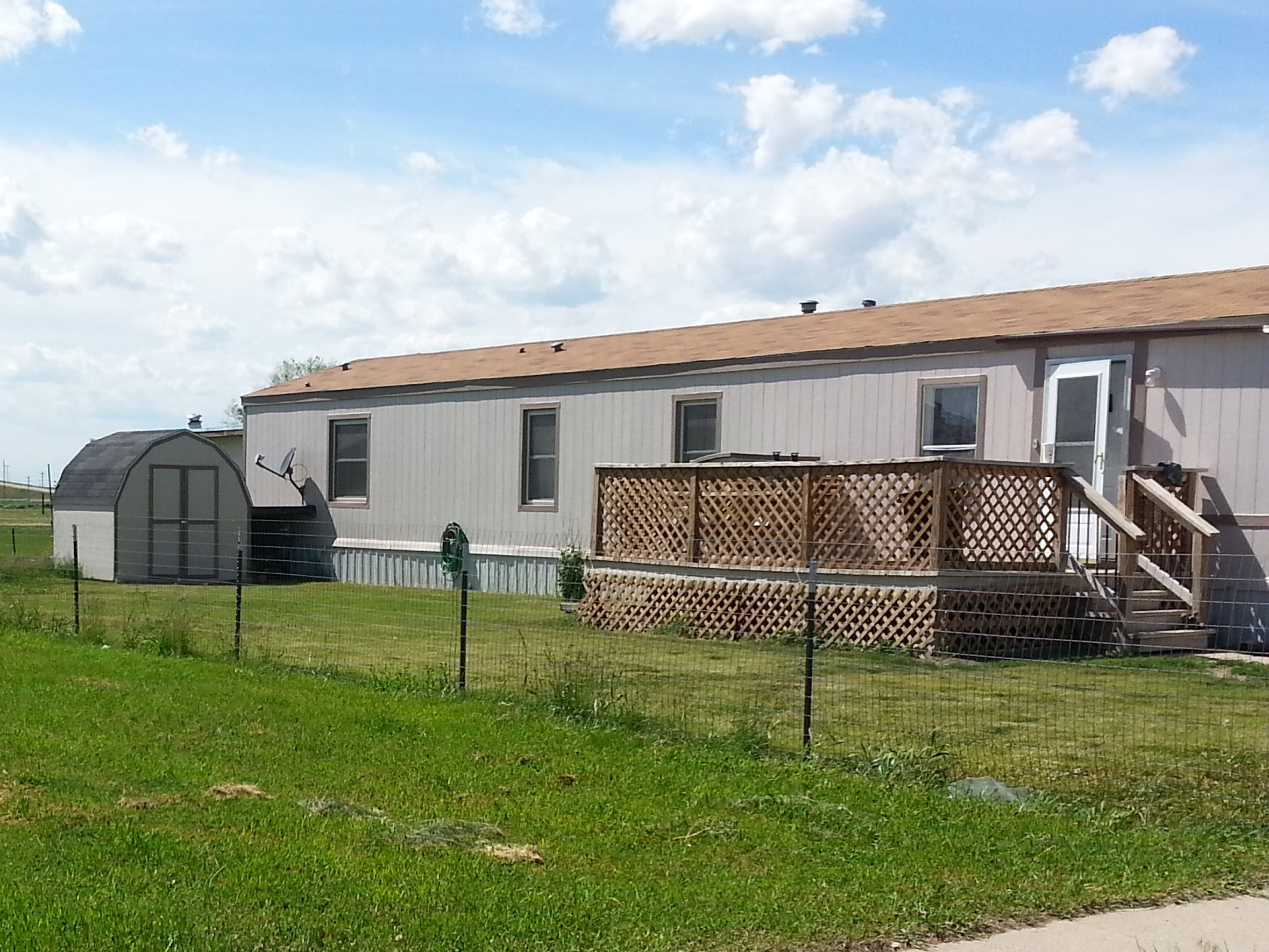 Occupied mobile home spot. Green grass and beautiful blue sky.